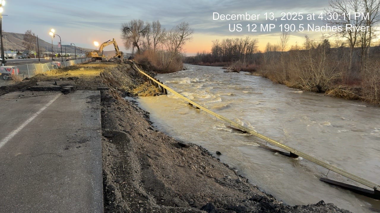 Workers with a backhoe attempt to fix a highway next to flooding river