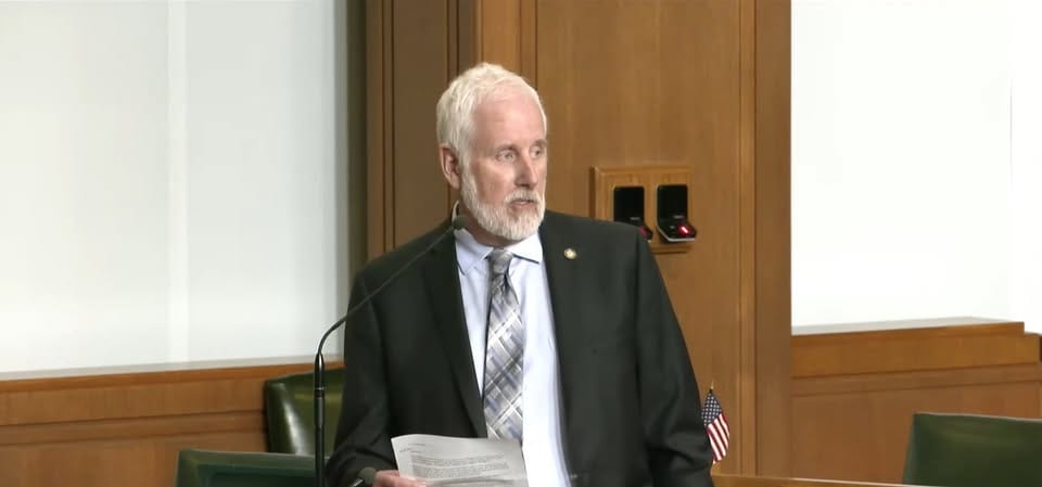 Rep Gamba in a tie and coat gives remarks in the legislature.