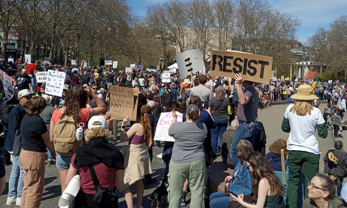 Protestors at a Hands Off protest at Seattle Center hold signs, including "RESIST" and "Could you imgaine if Obama did ANY of this?"