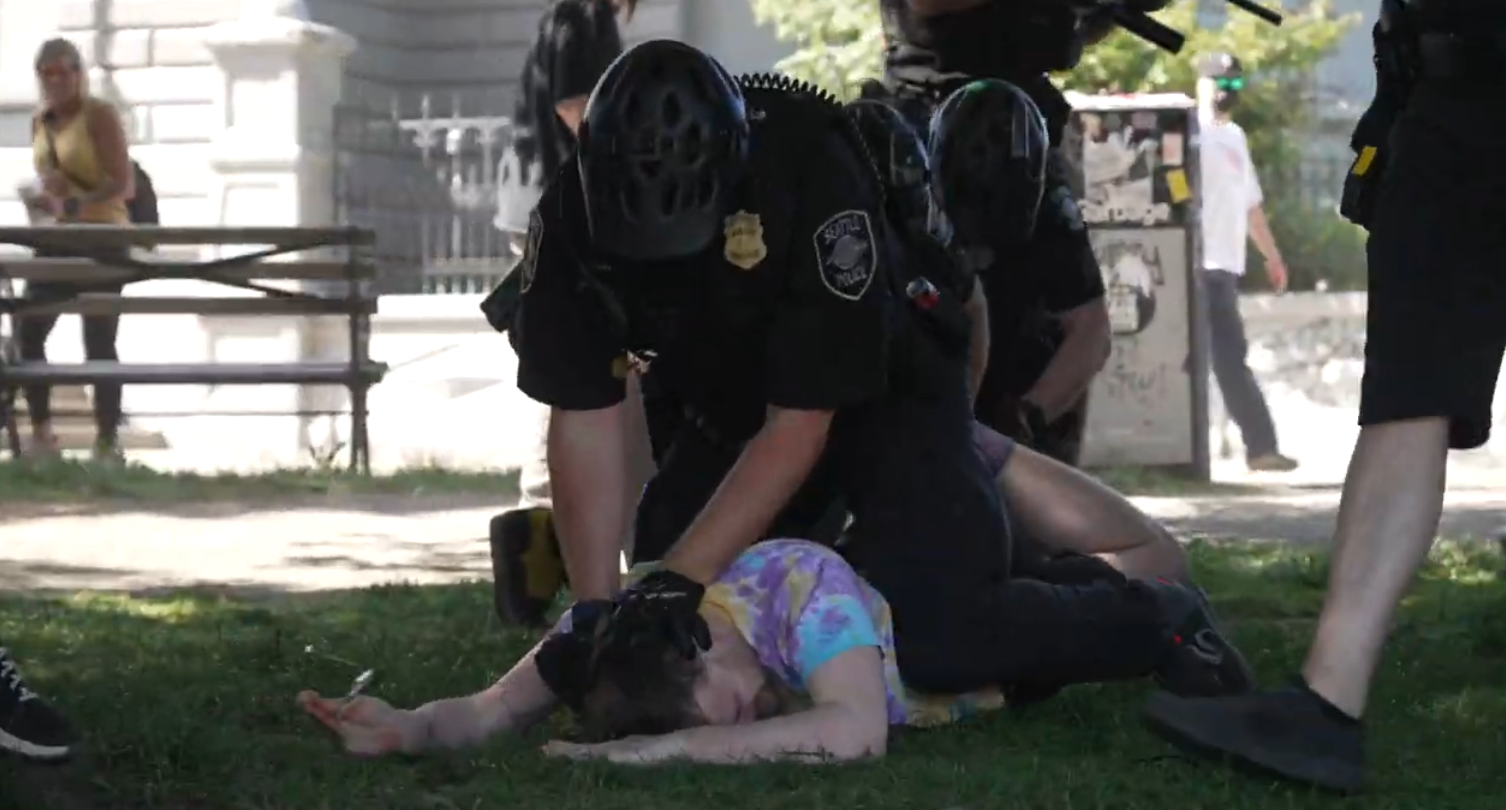 A Seattle Police Officer forcefully straddles and arrests someone wearing tie dye at a religious right wing protest in Seattle.