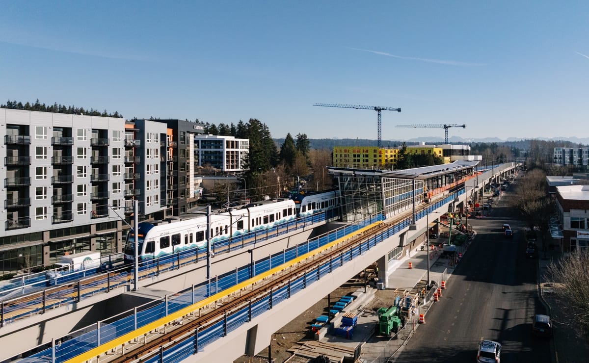 A light rail train enters a news Link station in Redmond Washington with apartments under construction in the background.