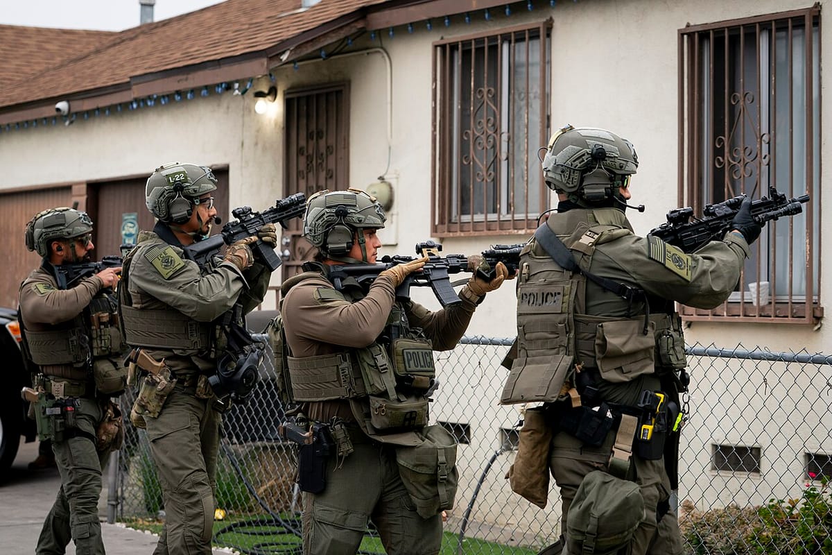 Four Immigration and Customs Enforcement agents, in full combat gear, point assault rifles at small home in Los Angeles.