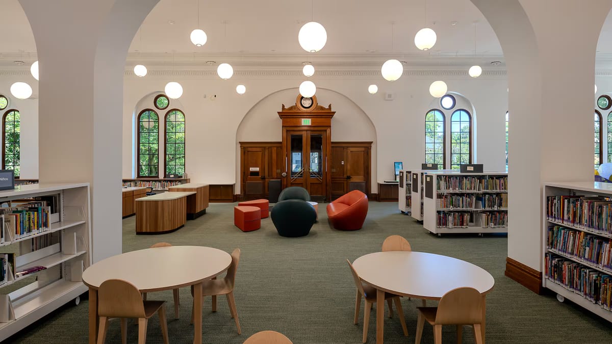 A library interior with children's tables, modern couches, arched windows and ornate wooden doors.
