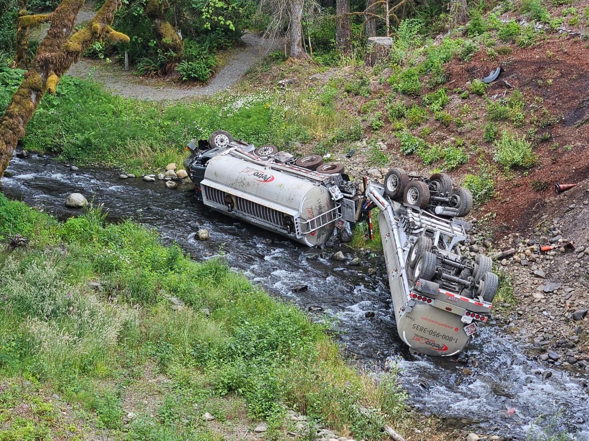 An overturned fuel truck spills gasoline into a creek.