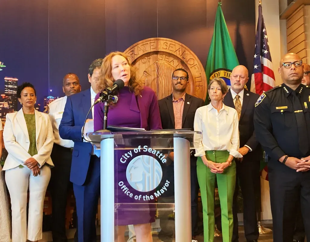 City attorney Ann Davison speaks to the media behind a podium that reads City of Seattle Office of the Mayor and stands next to ciity council members, the mayor and chief of police.