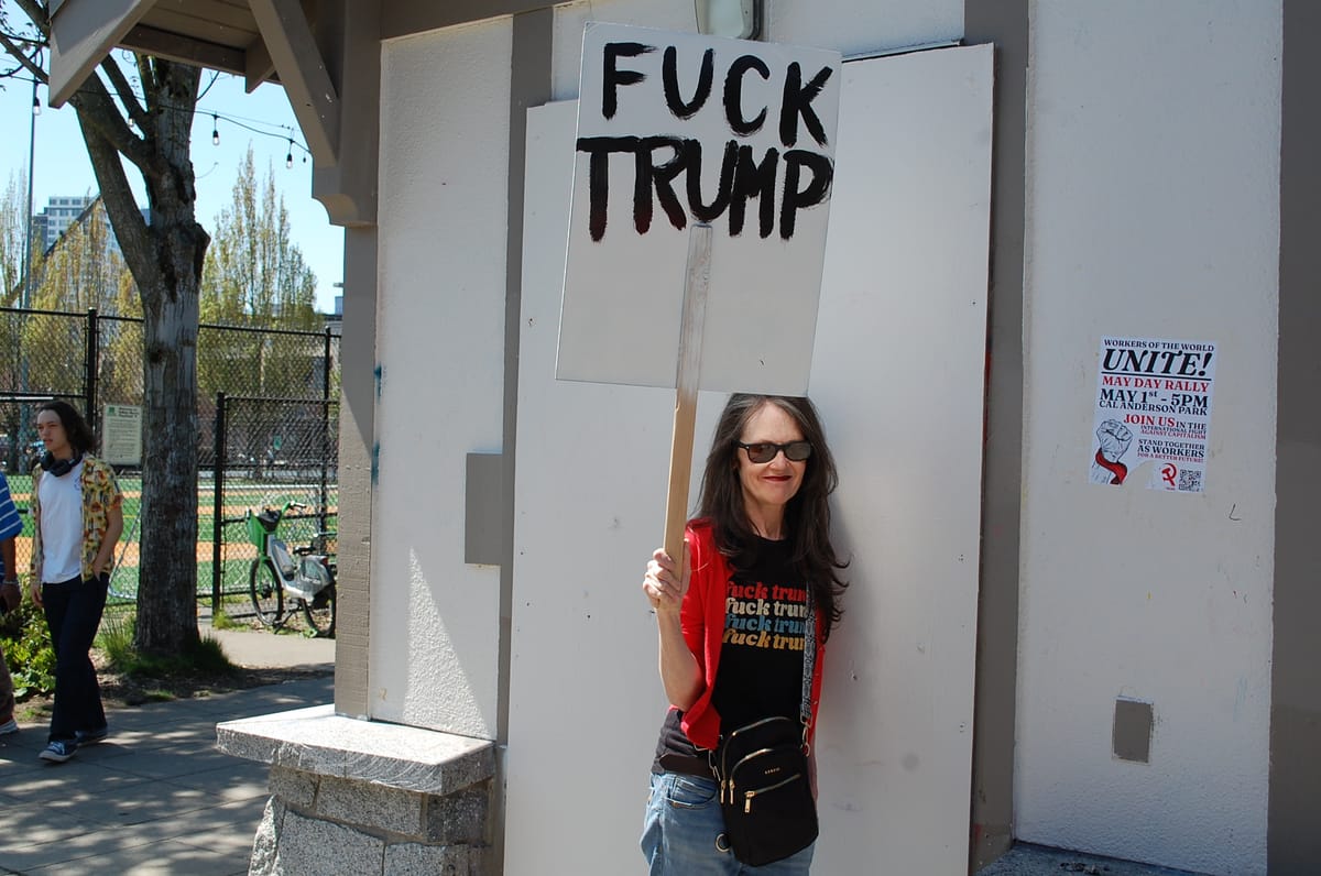 A woman wearing a t-shirt that says fuck trump four times holds a hand painted sign that reads: Fuck Trump.