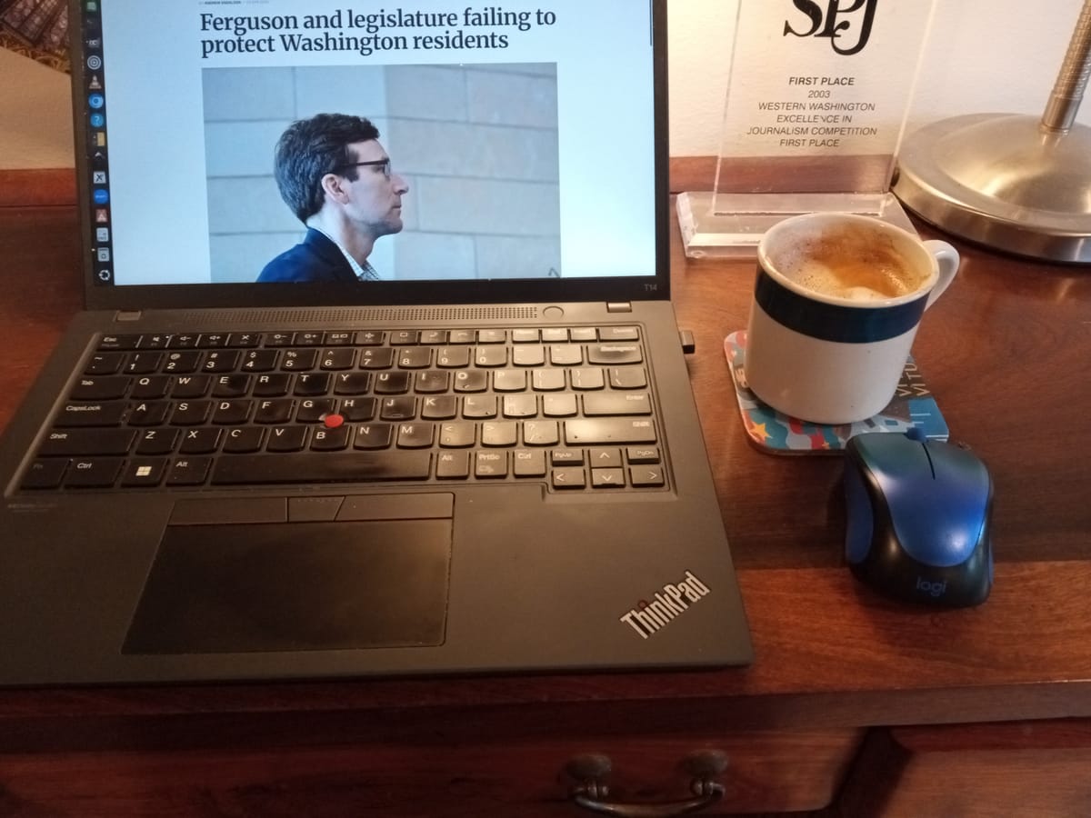 A laptop computer on a desk beside a cup of coffee and a journalism award. On the screen is an article with the headline Ferguson and legislature failing to protect Washington residens