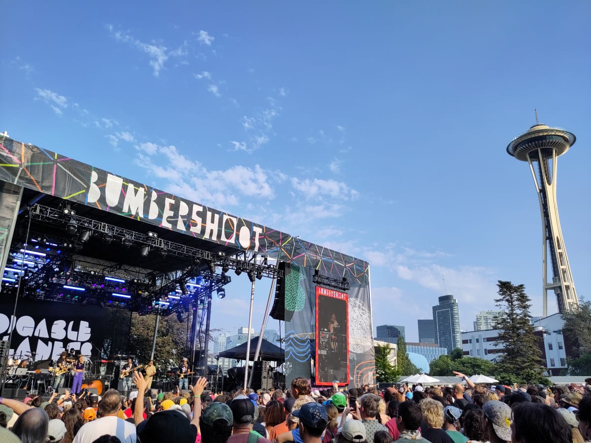 The hip hop goup Digable Planets plays on an outdoor stage in front of a large crowd with the Space Needle in the background.