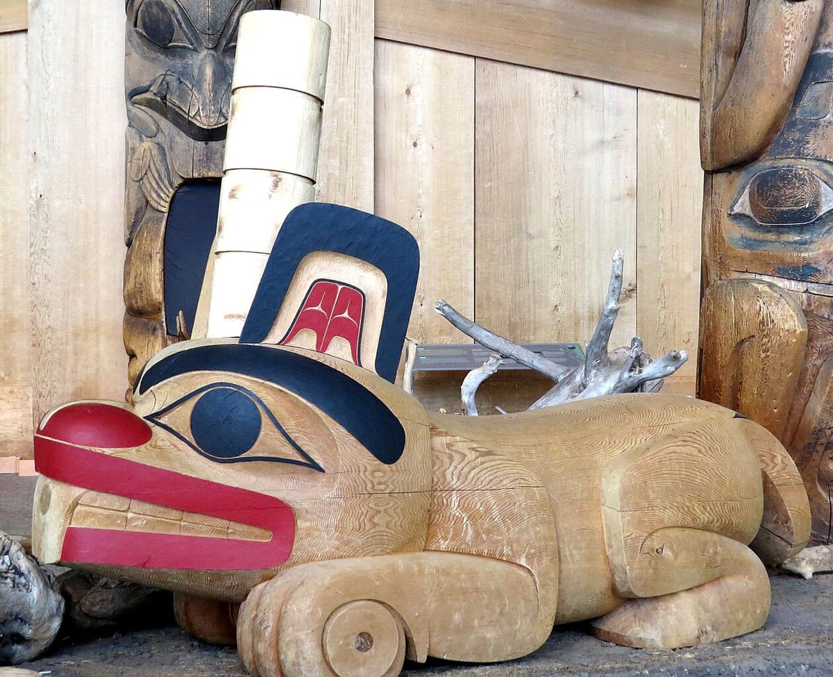 An Haida-style sculpture of a beaver in wood, with stylized eyes, mouth, teeth, and ceremonial hat.