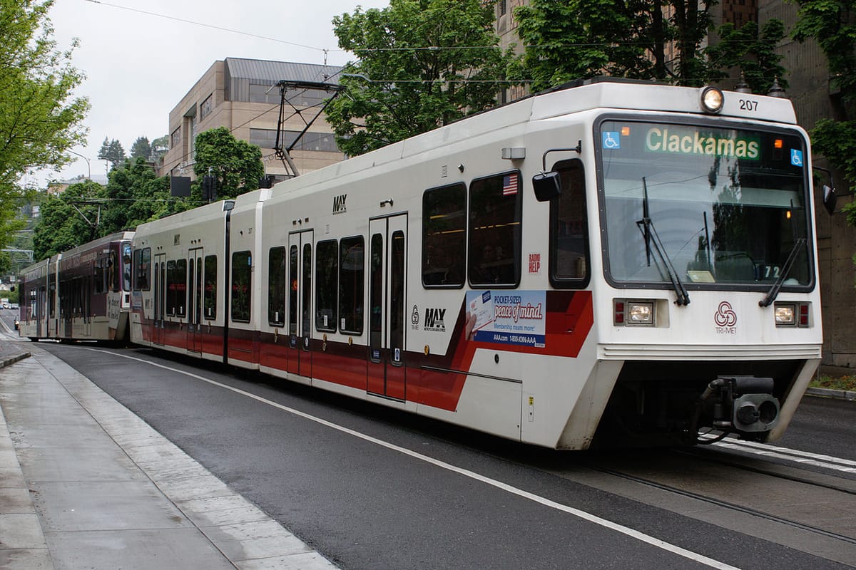 A red and white transit train travels on tracks on a urban road.