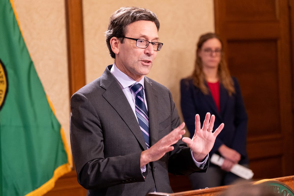 Governor Ferguson, in a suit with noticeable collar gap, gives a speech next to the Washingotn state flag.