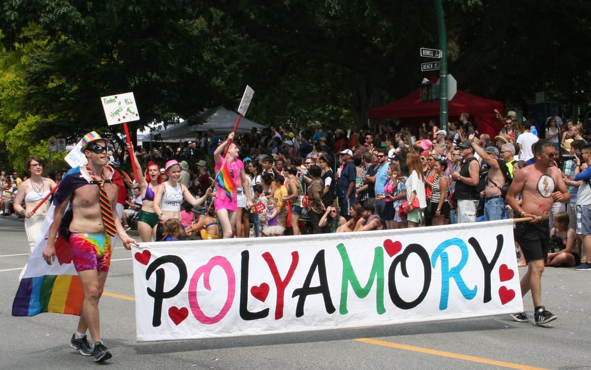 People march in a parade with colorful costumes and carrying a banner that reads: polyamory