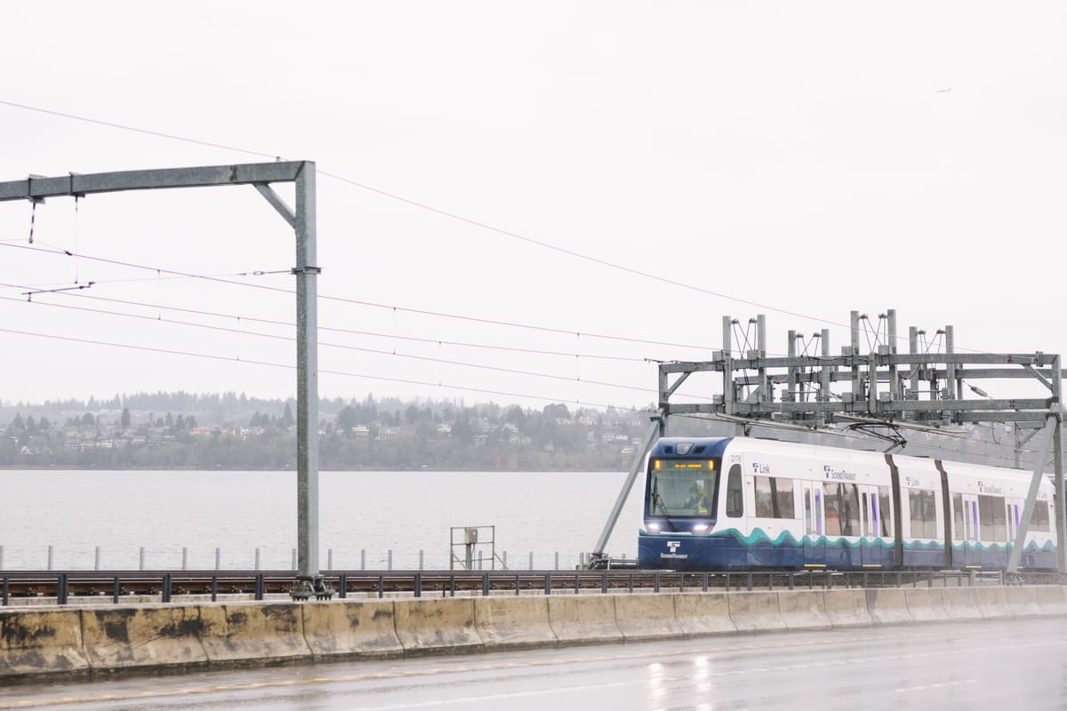 A light rail train crosses a lake on a floating bridge on a rainy day.