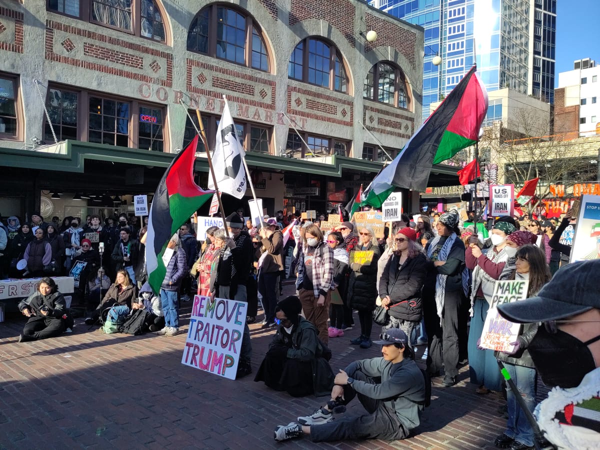 Protesters gather at Pike Place Market with Palestinian and Iranian flags and a sign that reads Remove Traitor Trump.