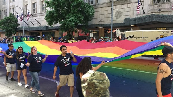 People marching in the Seattle Pride parade carry a large rainbow flag.