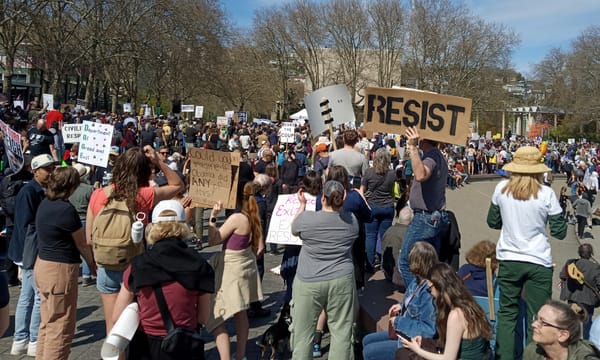 Protestors at a Hands Off protest at Seattle Center hold signs, including "RESIST" and "Could you imgaine if Obama did ANY of this?"