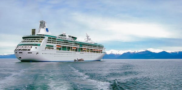 A cruise ship sails in front of snow-capped mountains.
