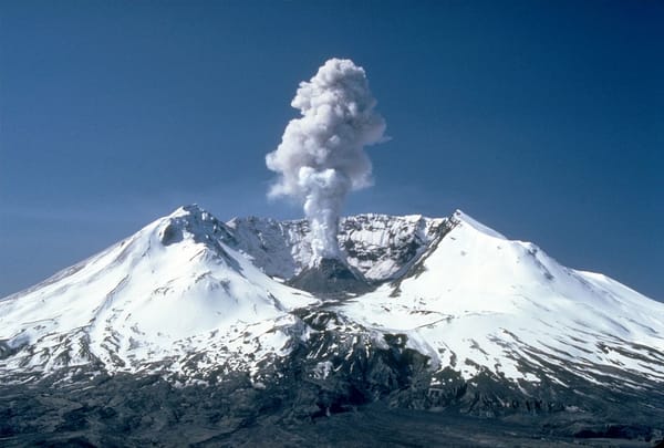 Mount St Helens, with a wide open crater, sends up a plume of steam from the growing volcanic dome at the center of the crater. The mountain is covered in snow.