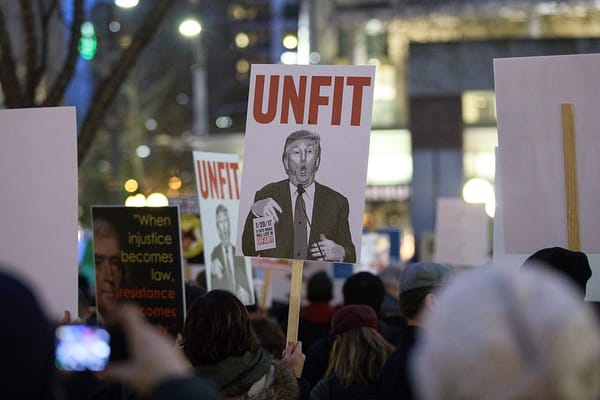 At a night time protest in Seattle's Westlake park, protesters hold signs including one of Donald Trump that reads "UNFIT."