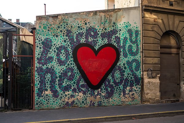 Street art on outdoor wall in San Antonio with a red heart and the words Love Thy Neighbor surrounding the heart.
