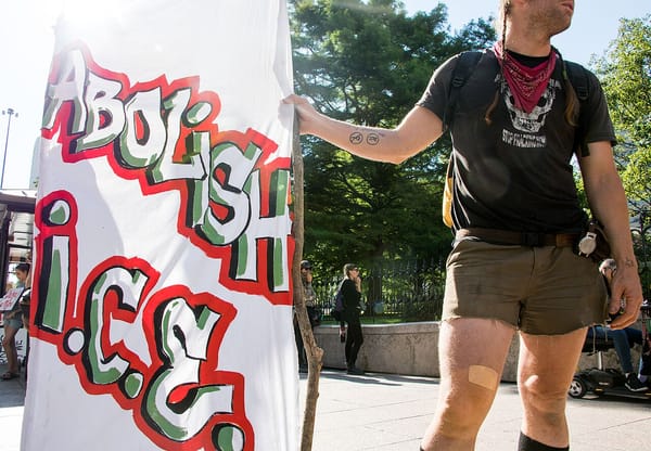A protester wearing T-Shirt with a skull image holds a handmade sign the reads Abolish ICE.