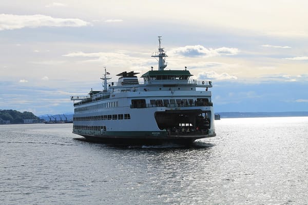 Washington state ferry Wenatchee sails on Puget Sound with port of Seattle cranes in the background.