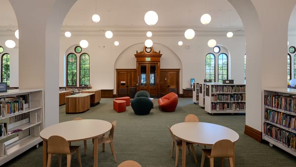 A library interior with children's tables, modern couches, arched windows and ornate wooden doors.