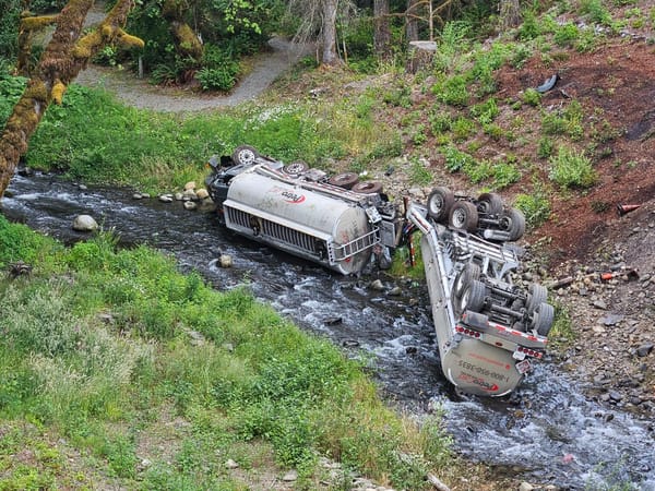 An overturned fuel truck spills gasoline into a creek.