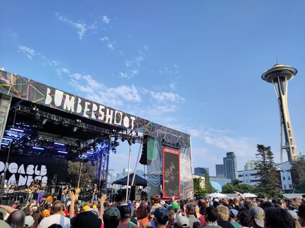 The hip hop goup Digable Planets plays on an outdoor stage in front of a large crowd with the Space Needle in the background.