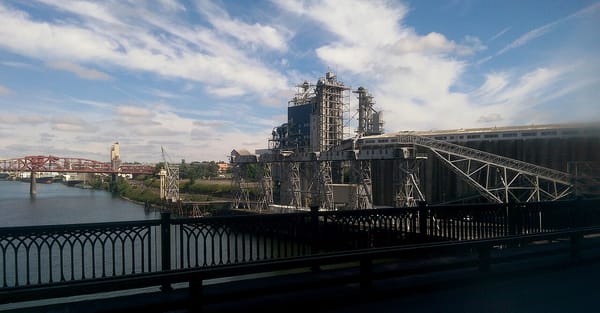A grain terminal and aging industrial equipment beside a river and bridge.