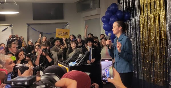 Katie Wilson faces a crowd of supporters and photographers with a microphone in her hand.