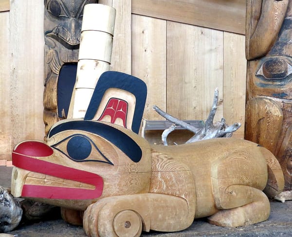 An Haida-style sculpture of a beaver in wood, with stylized eyes, mouth, teeth, and ceremonial hat.