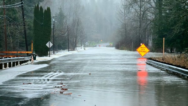 Flood waters flow over a rural road with a sign reading Water Over Roadway