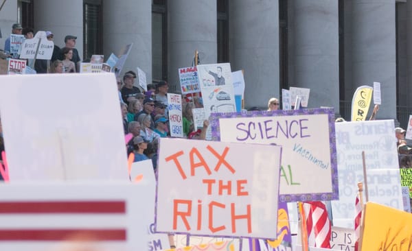 Signs on the steps of the capitol building in Olympia, including one in the foreground that reads: tax the rich