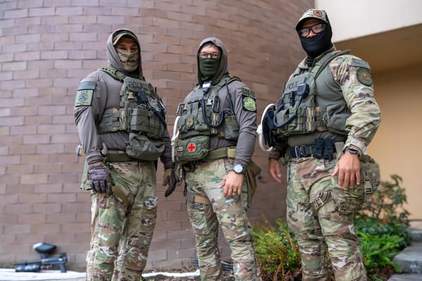 Three cowardly goons in camoflauge and tactical gear hide their faces under neck gaiters.