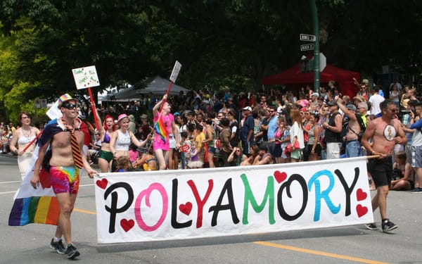 People march in a parade with colorful costumes and carrying a banner that reads: polyamory
