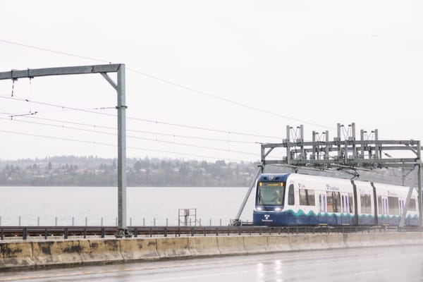 A light rail train crosses a lake on a floating bridge on a rainy day.